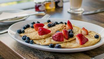 A breakfast plate with pancakes, strawberries, and blueberries, a glass of milk, and a jar of jam on a wooden table.