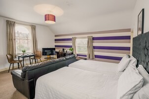 Habitación de hotel con una cama grande, un sofá cama, un escritorio con silla, un televisor y una ventana con cortinas.