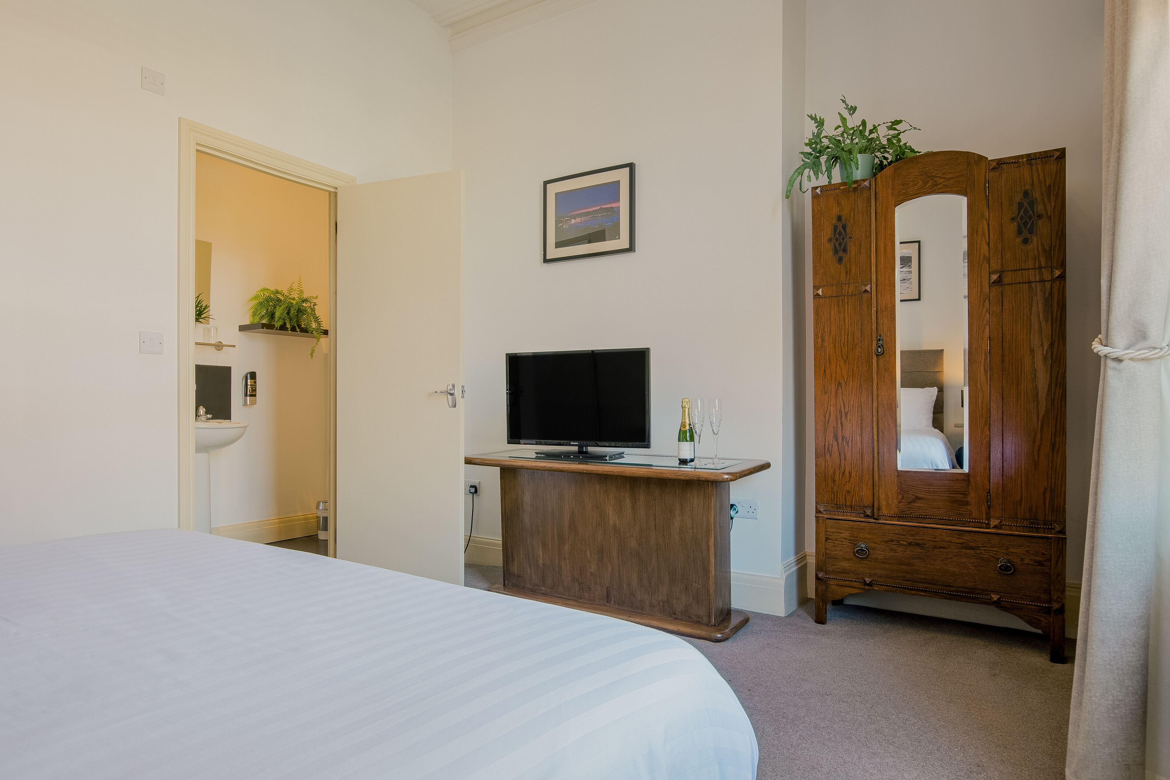 Una habitación de hotel con una cama, un tocador de madera, un televisor, un lavamanos y un espejo.