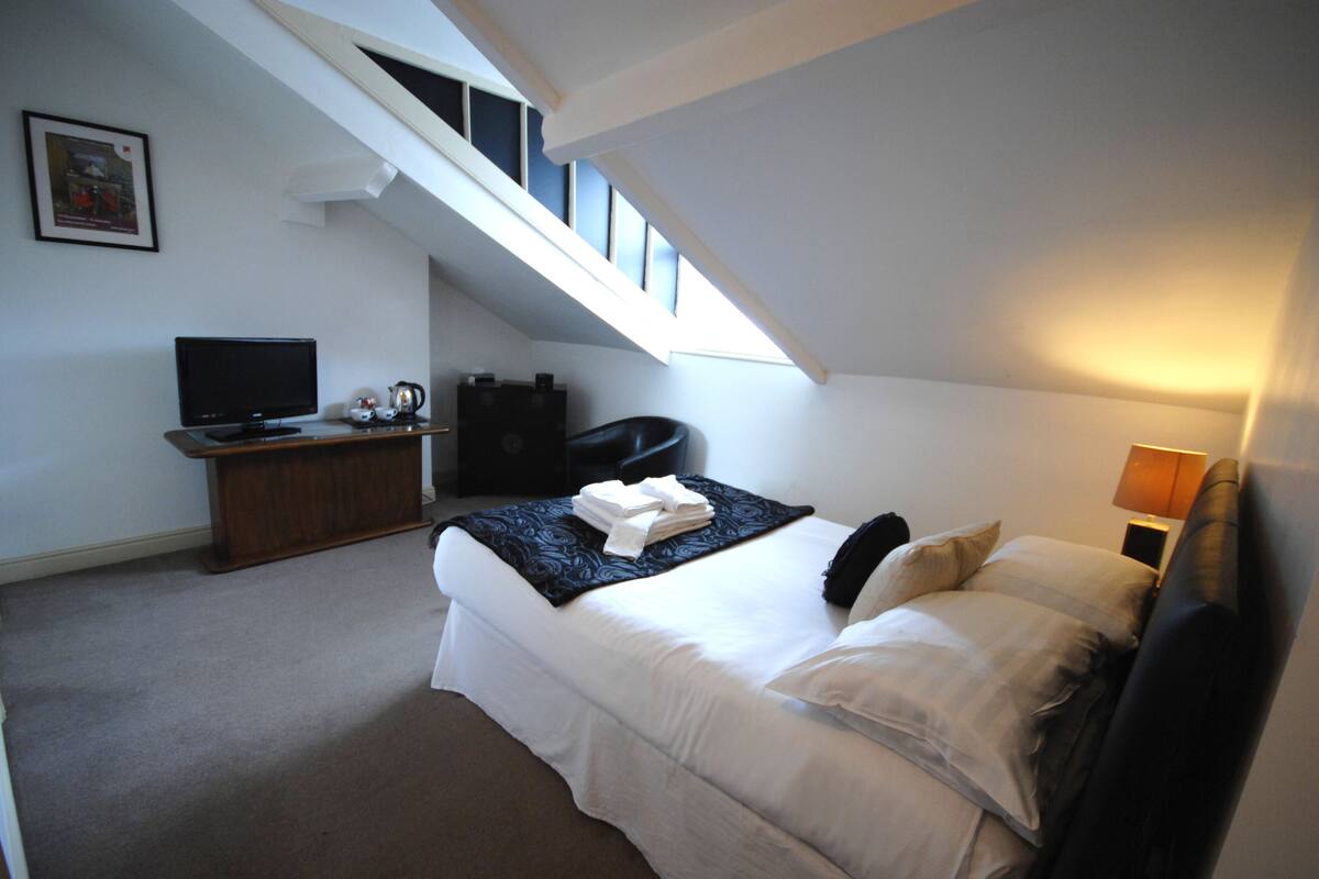 A bedroom with a bed, a desk, a television, and a window.