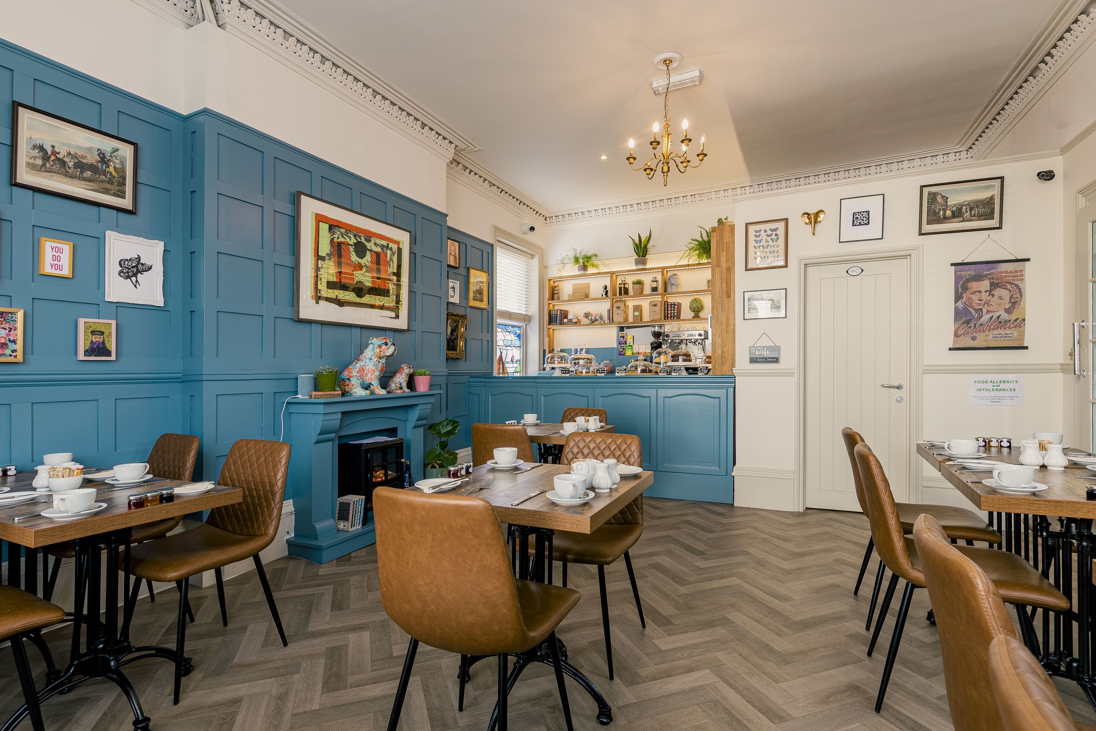 A dining area with blue paneled walls, a fireplace, and a variety of framed pictures and decorations.