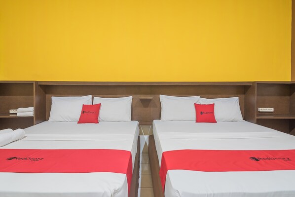 A hotel room with two beds, each with white bedding and red accents, and a bright yellow wall. - RedDoorz near Alun Alun Subang (Subang)