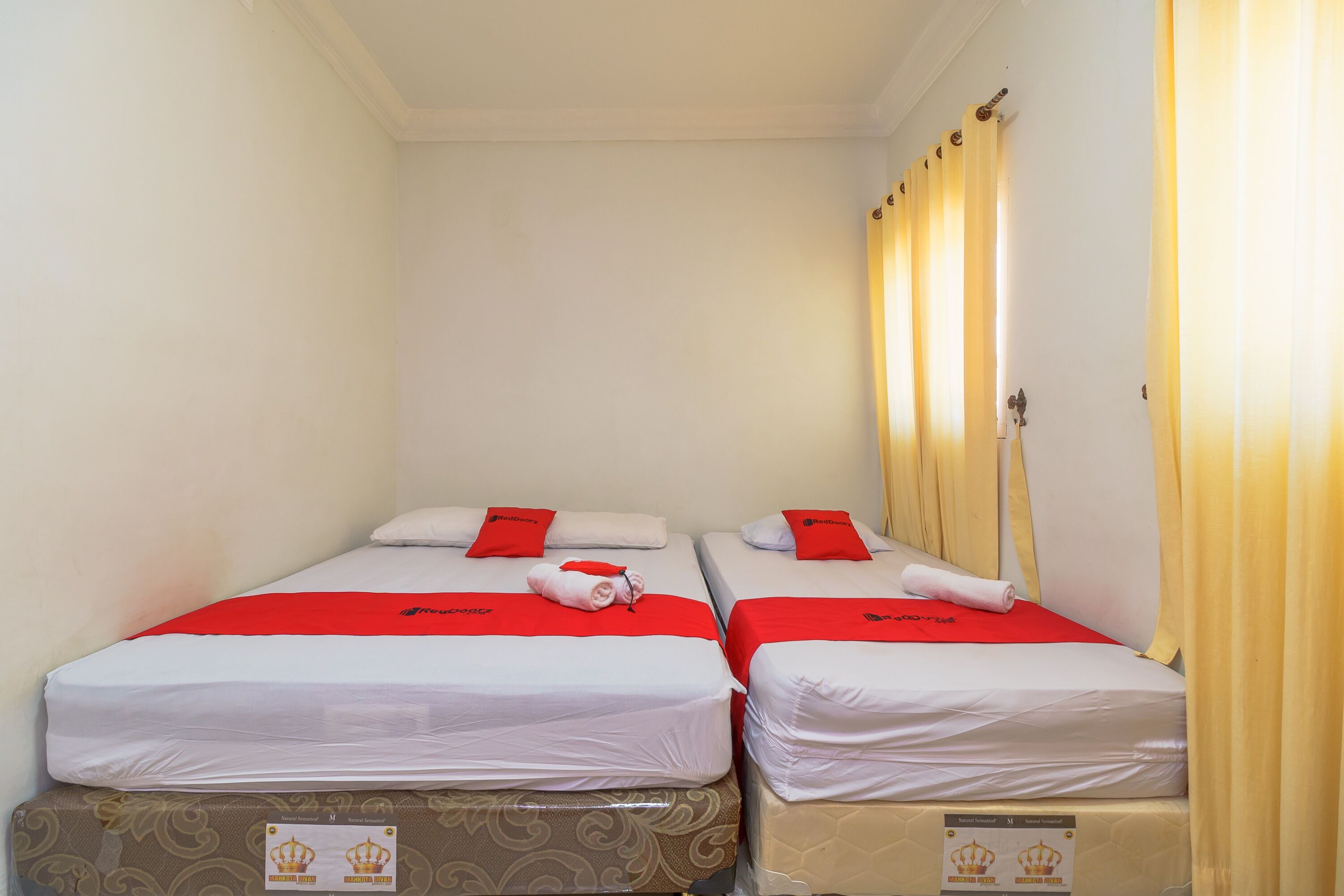 Two single beds with red and white bedding, a patterned mattress cover, and a curtain on the right.