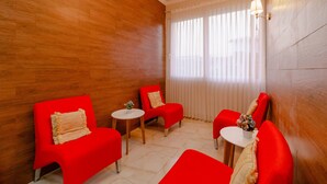 Ein Zimmer mit Holzwandverkleidung, einem roten Sofa, einem kleineren roten Sessel, einem runden Tisch und einem Fenster mit Vorhängen.