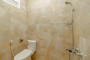 A bathroom with a toilet, a shower, and a marble wall.
