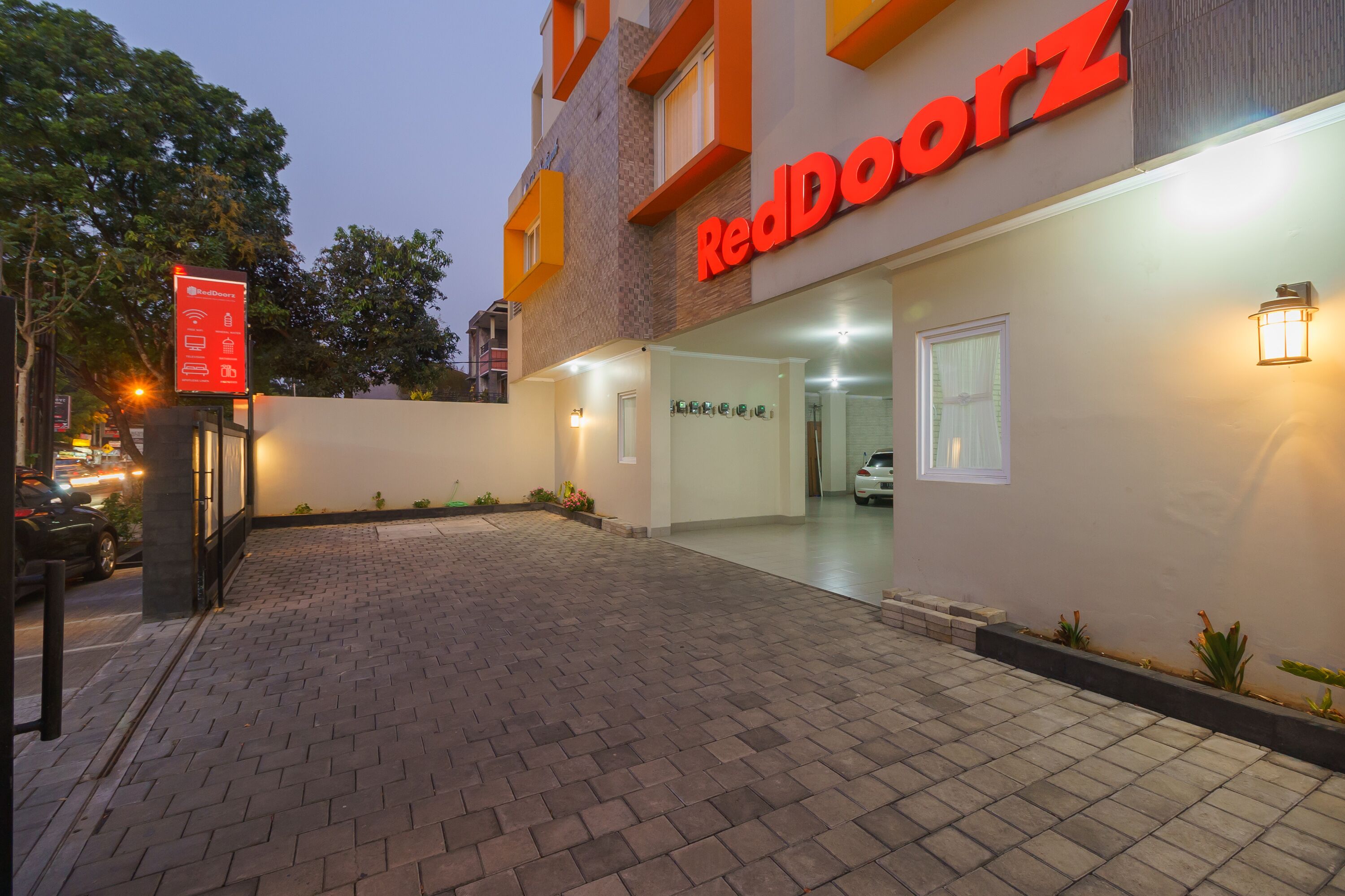 Entrada de un hotel RedDoorz con un camino pavimentado, un cartel y una fachada bien iluminada.