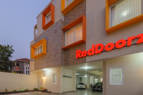 A building with a sign reading "RedDoorz" and a parking area with cars.