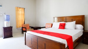 Ein Hotelzimmer mit einem hölzernen Bett, einer roten Decke, einem Wasserspender, einem Sessel und einem kleinen Tisch.