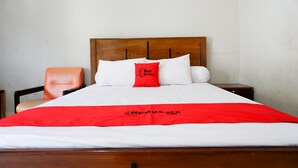 Ein ordentlich bezogenes Bett mit einer roten und weißen Tagesdecke, einem hölzernen Kopfteil und einem einzelnen roten Kopfkissen mit dem Aufdruck "Red Doorz".