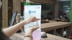 Une personne utilise un distributeur de gel hydroalcoolique au comptoir d'accueil d'un hôtel.