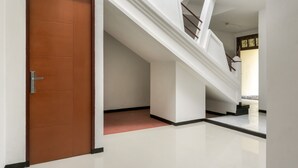 A hallway with a wooden door, a staircase, and a tiled floor. - RedDoorz near Universitas Widyagama Malang (Malang)