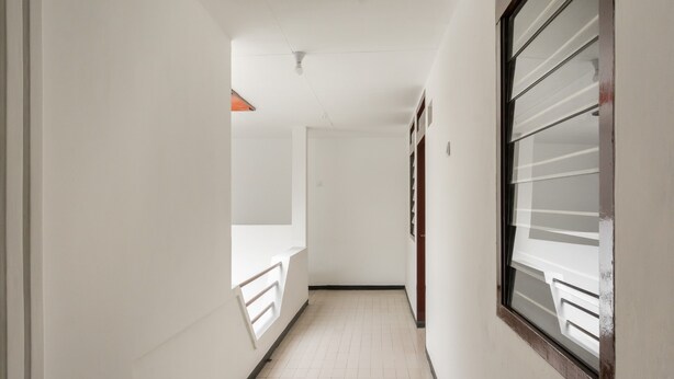 A narrow hallway with white walls, a tiled floor, and a window with blinds. - RedDoorz near Universitas Widyagama Malang (Malang)