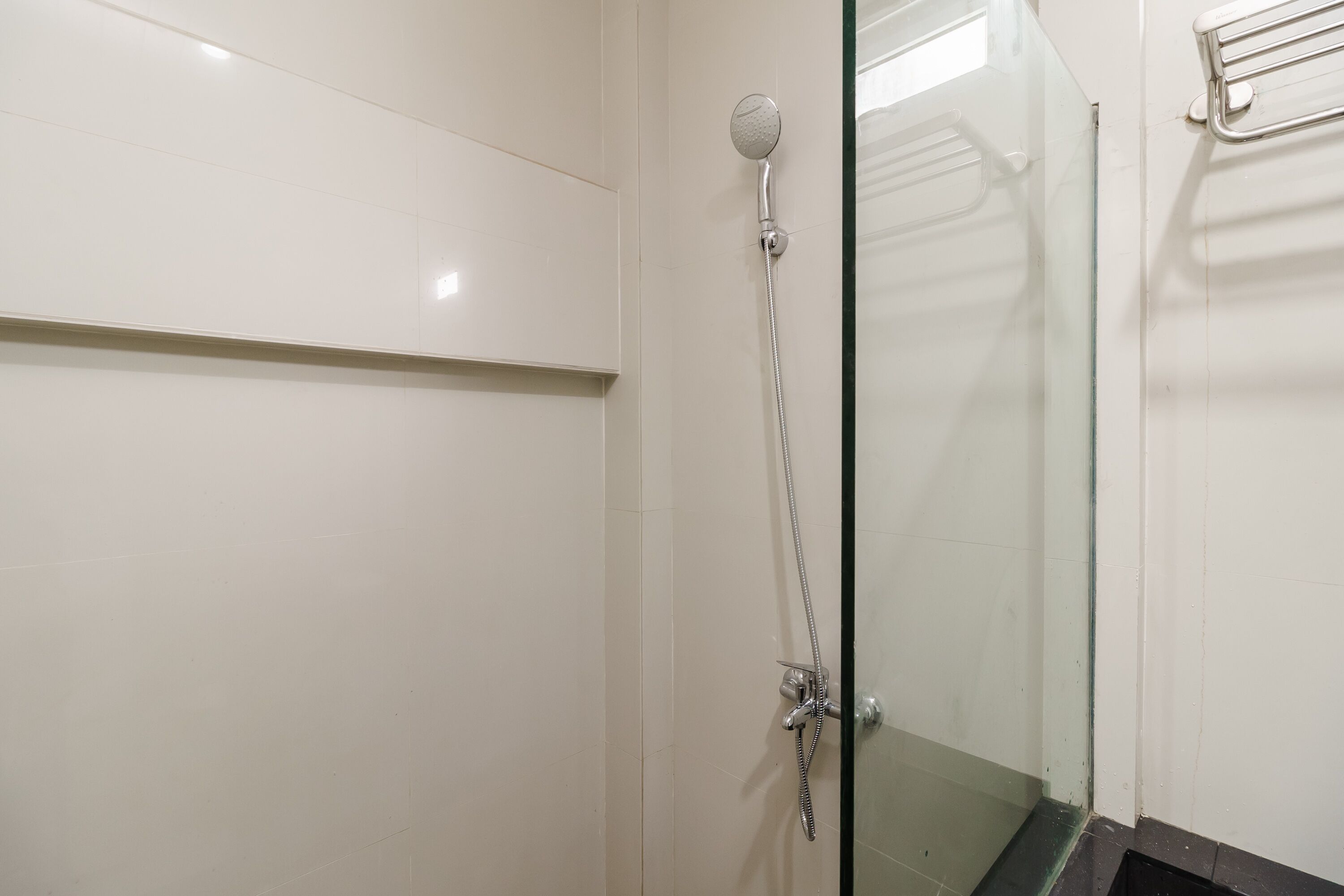 Un área de ducha con paredes de vidrio, un cabezal de ducha de mano y un grifo instalado en la pared.
