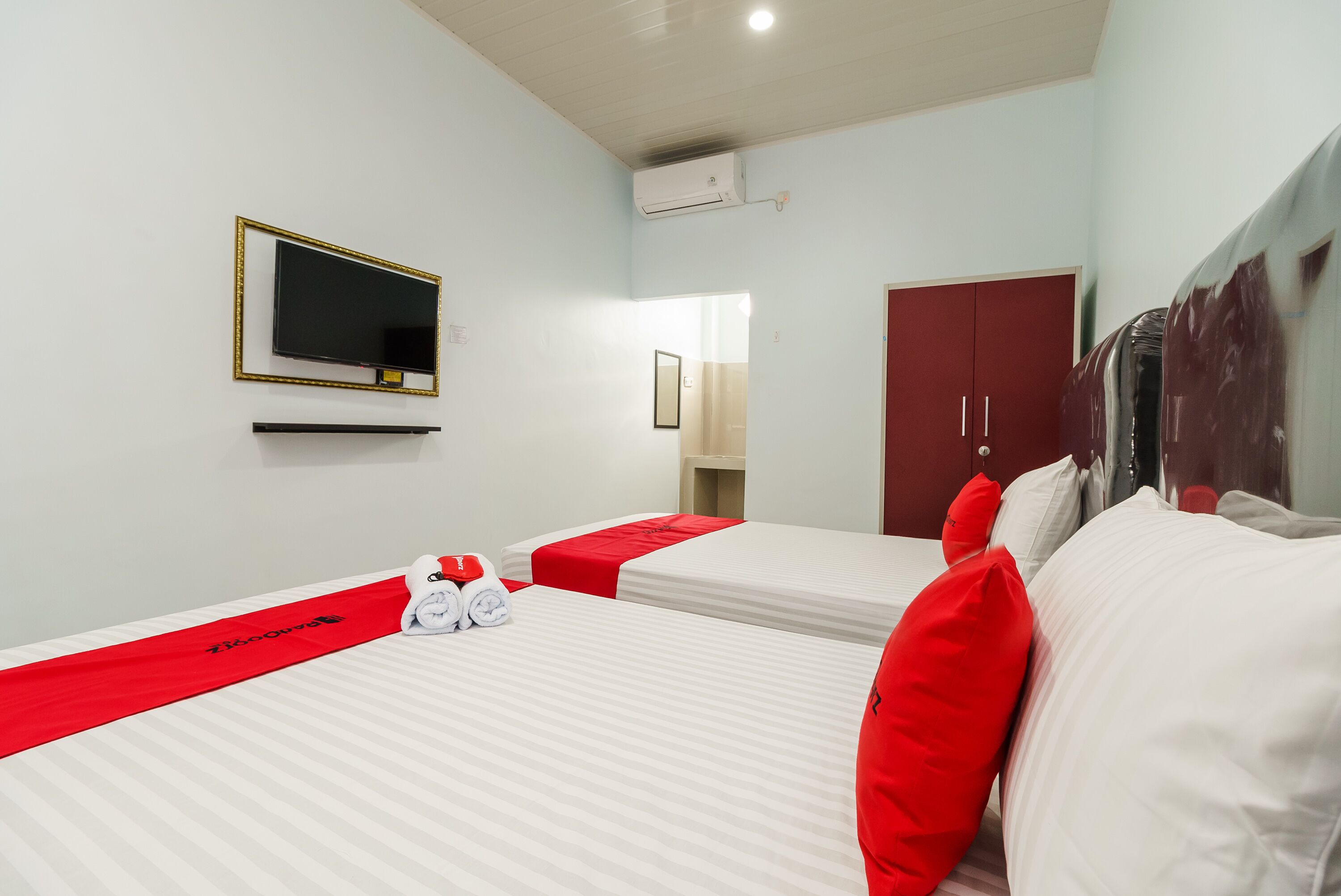 A hotel room with two beds, a TV, a wardrobe, and a bathroom.