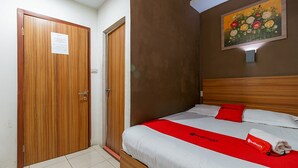 Ein Hotelzimmer mit Holztür, einem Bett mit weißer Bettwäsche und roten Akzenten sowie einem floralen Gemälde an der Wand.