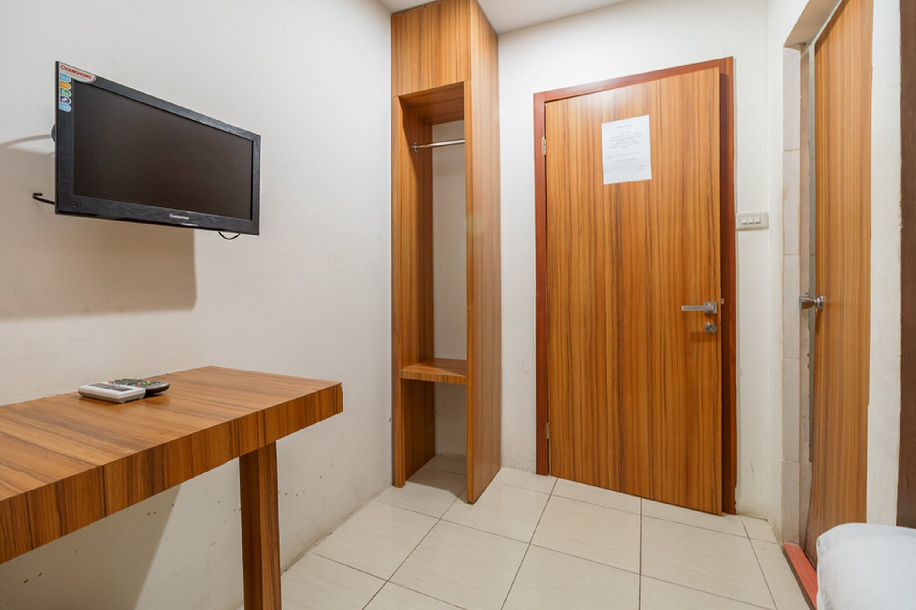 Una habitación con escritorio de madera, televisor montado en la pared, armario de madera y suelo de baldosas.