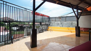 Un espacio al aire libre cubierto, con barandilla de metal, escalera y suelo de baldosas.