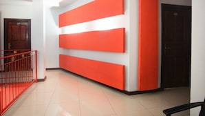 Un pasillo con barandilla roja, una puerta de madera y una pared con tres paneles rojos.