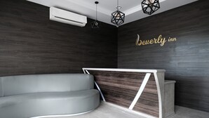 Un espace d’accueil moderne avec un canapé gris aux lignes courbes, un comptoir d’accueil en bois et un mur en bois foncé.