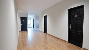 Un couloir doté d’un plancher en bois, de portes noires et de murs blancs.