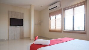 Une chambre d’hôtel avec un lit, un téléviseur à écran plat fixé au mur et deux fenêtres équipées de stores.