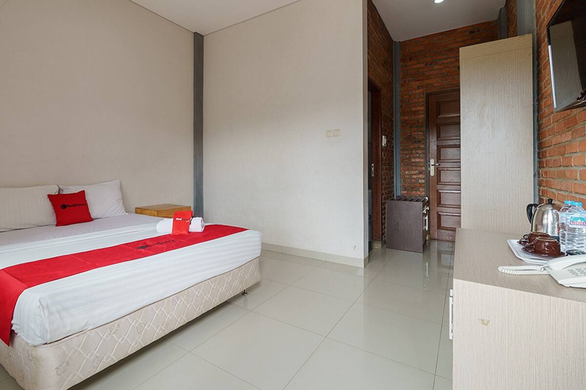 A hotel room with a bed, a desk with a telephone, and a brick wall.