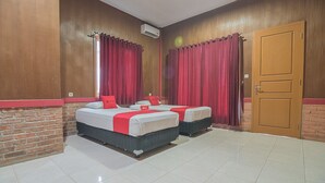 A hotel room with two beds, red curtains, a wooden door, and a brick accent wall.