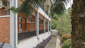 A multi-story building with a brick facade, balconies, and a paved pathway lined with plants.