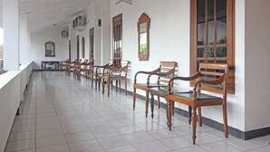 A long corridor with wooden chairs and tables, white walls, and large windows. - RedDoorz Plus @ Taman Siswa 3 (Yogyakarta)