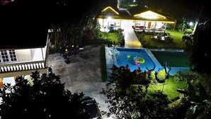 A hotel with a swimming pool, a covered patio, and a well-lit garden area at night. - Residences by RedDoorz near Taman Safari (Cisarua)