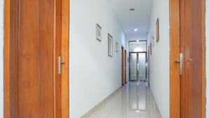Un pasillo largo y estrecho con puertas de madera a ambos lados y suelo de baldosas.
