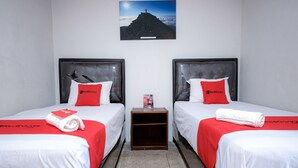 A hotel room with two beds, each with a red and white bedspread, a small wooden nightstand, and a framed picture on the wall. - RedDoorz @ Cempaka Putih Jambi (Jambi)