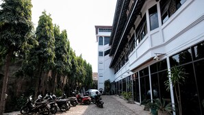 A courtyard with motorcycles parked along the left side, a building with large windows on the right, and potted plants. - RedDoorz @ Cempaka Putih Jambi (Jambi)