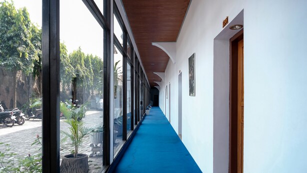 A corridor with a blue carpet, large windows, and potted plants. - RedDoorz @ Cempaka Putih Jambi (Jambi)