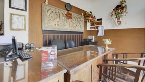 A reception area with a wooden reception desk, black chairs, a clock, framed certificates, and a decorative wall piece.