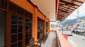 A covered balcony with wooden chairs, a sign reading "HANDINI," and a view of a street with buildings and mountains in the background. - RedDoorz near Sarangan Lake (Plaosan)