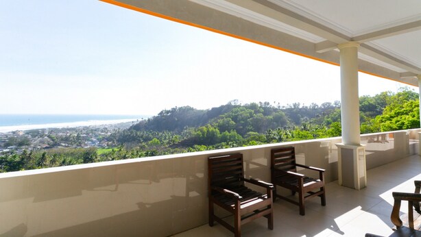 A balcony with two wooden chairs and a table, overlooking a coastal landscape with greenery and a view of the sea. - RedDoorz near Parangtritis Beach (Parangtritis)