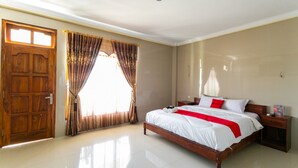 A spacious bedroom with a large bed, a wooden door, and curtains. - RedDoorz near Parangtritis Beach (Parangtritis)
