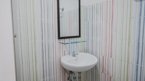 Een badkamer met een wit wastafel, een spiegel en gestreepte tegels.