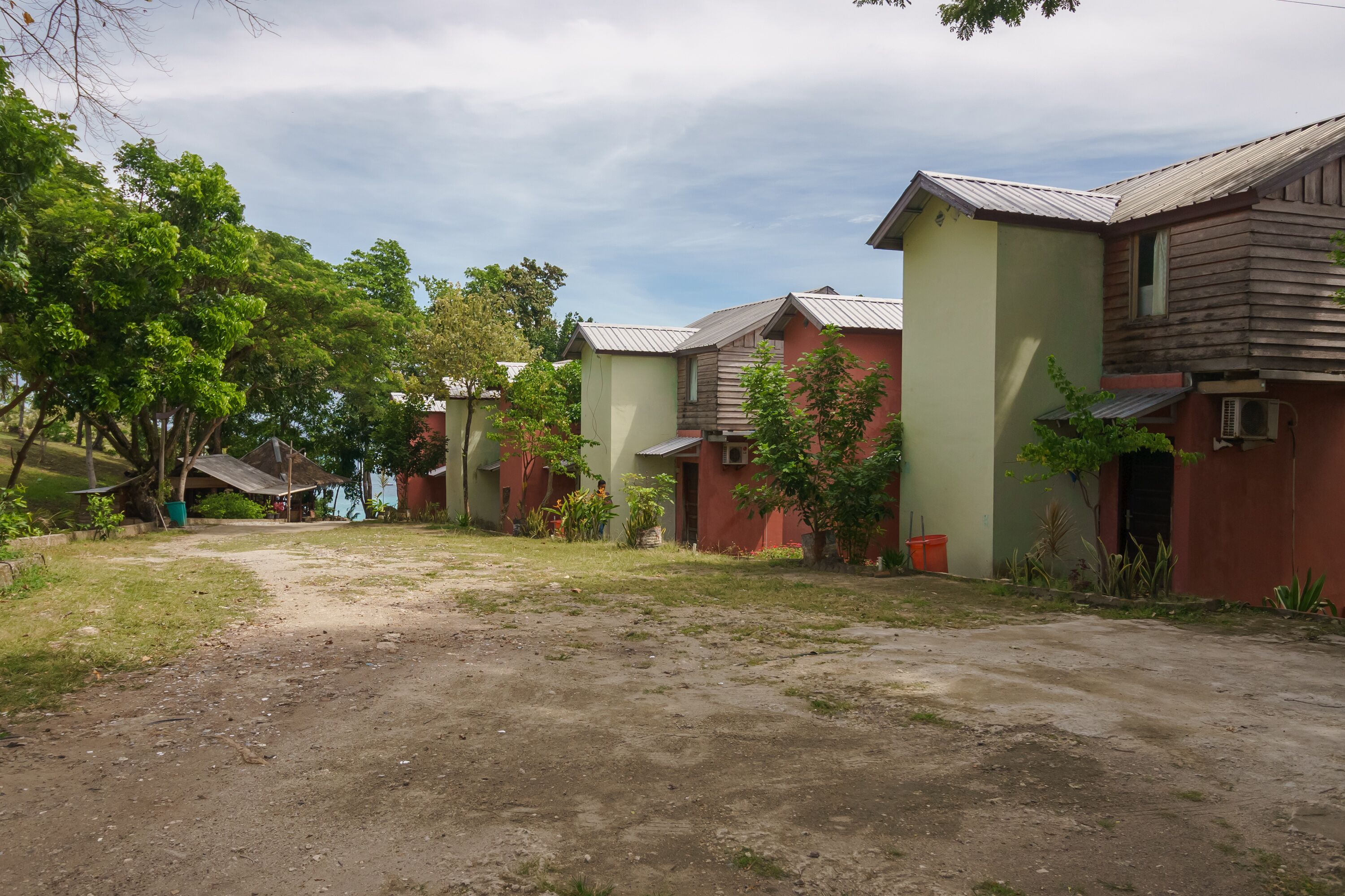 Una hilera de casas de madera con paredes verdes y techos metálicos, rodeadas de árboles y un sendero de tierra.