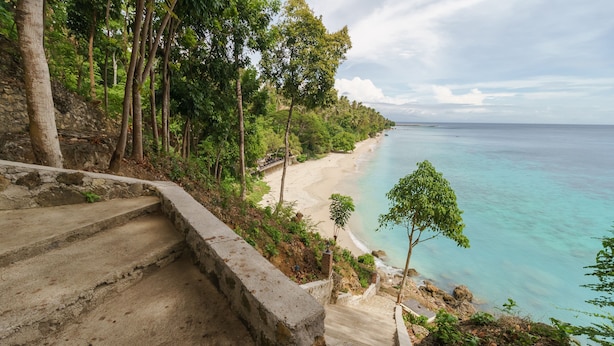 Un escalier menant à une plage bordée d’une eau turquoise cristalline et d’une végétation luxuriante.