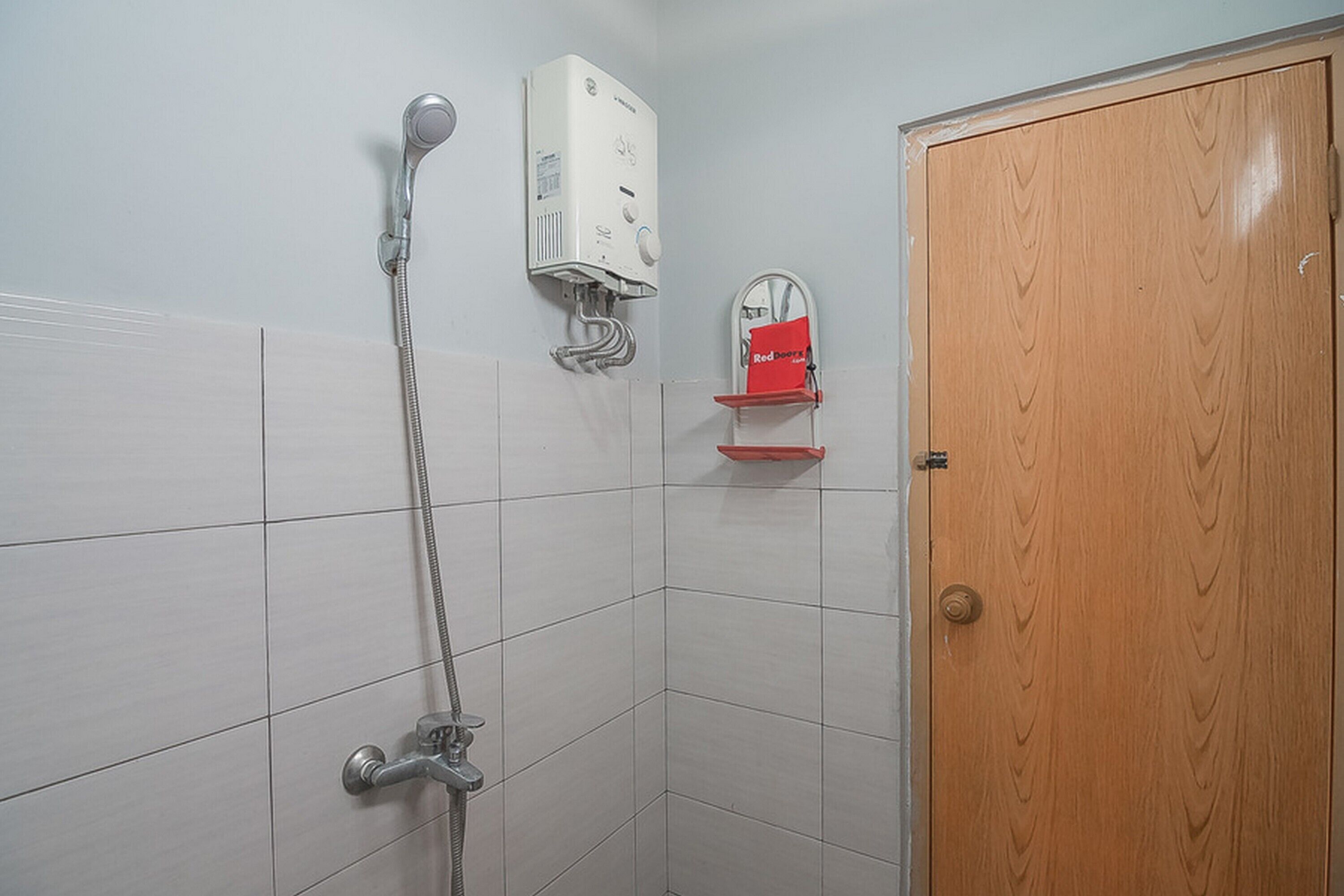 Un área de ducha con cabezal de ducha de mano, calentador de pared y dispensador de jabón rojo.