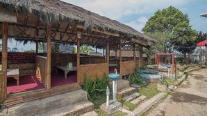 A rustic wooden structure with a thatched roof, outdoor seating, and a small water fountain. - RedDoorz near Happy Farm Ciwidey (Rancabali)