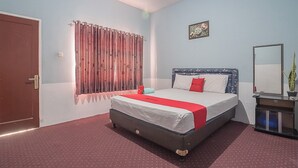 A hotel room with a bed, curtains, a bedside table, a mirror, and a door. - RedDoorz near Happy Farm Ciwidey (Rancabali)