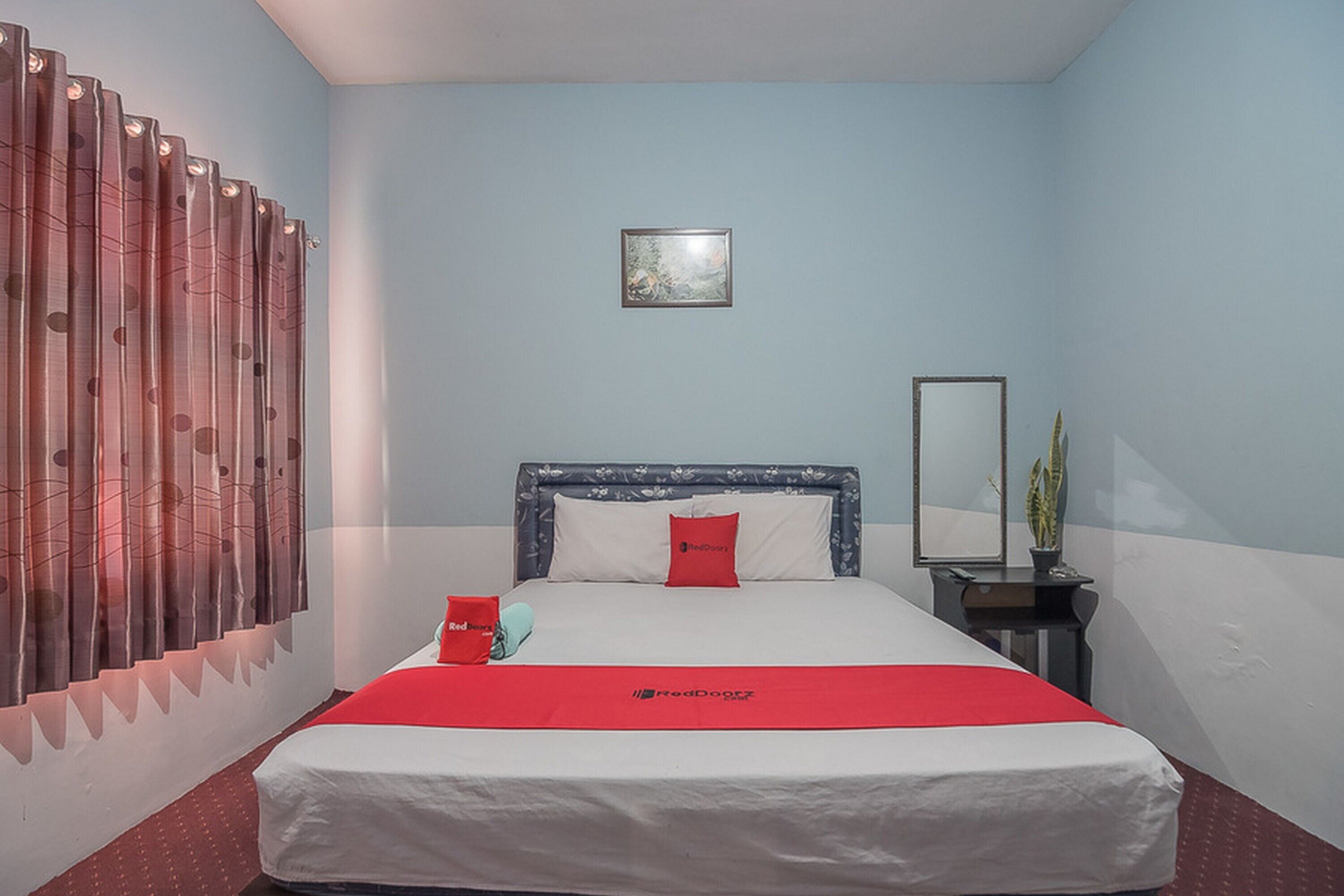 A hotel room with a bed, a nightstand, a mirror, and a window with curtains.