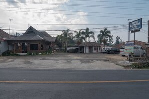 A parking lot with several buildings, including a two-story structure with a sloped roof and a smaller building with a red door. - RedDoorz near Happy Farm Ciwidey (Rancabali)