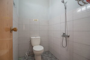 A small, tiled bathroom with a toilet, a shower, and a wooden door. - RedDoorz near Happy Farm Ciwidey (Rancabali)