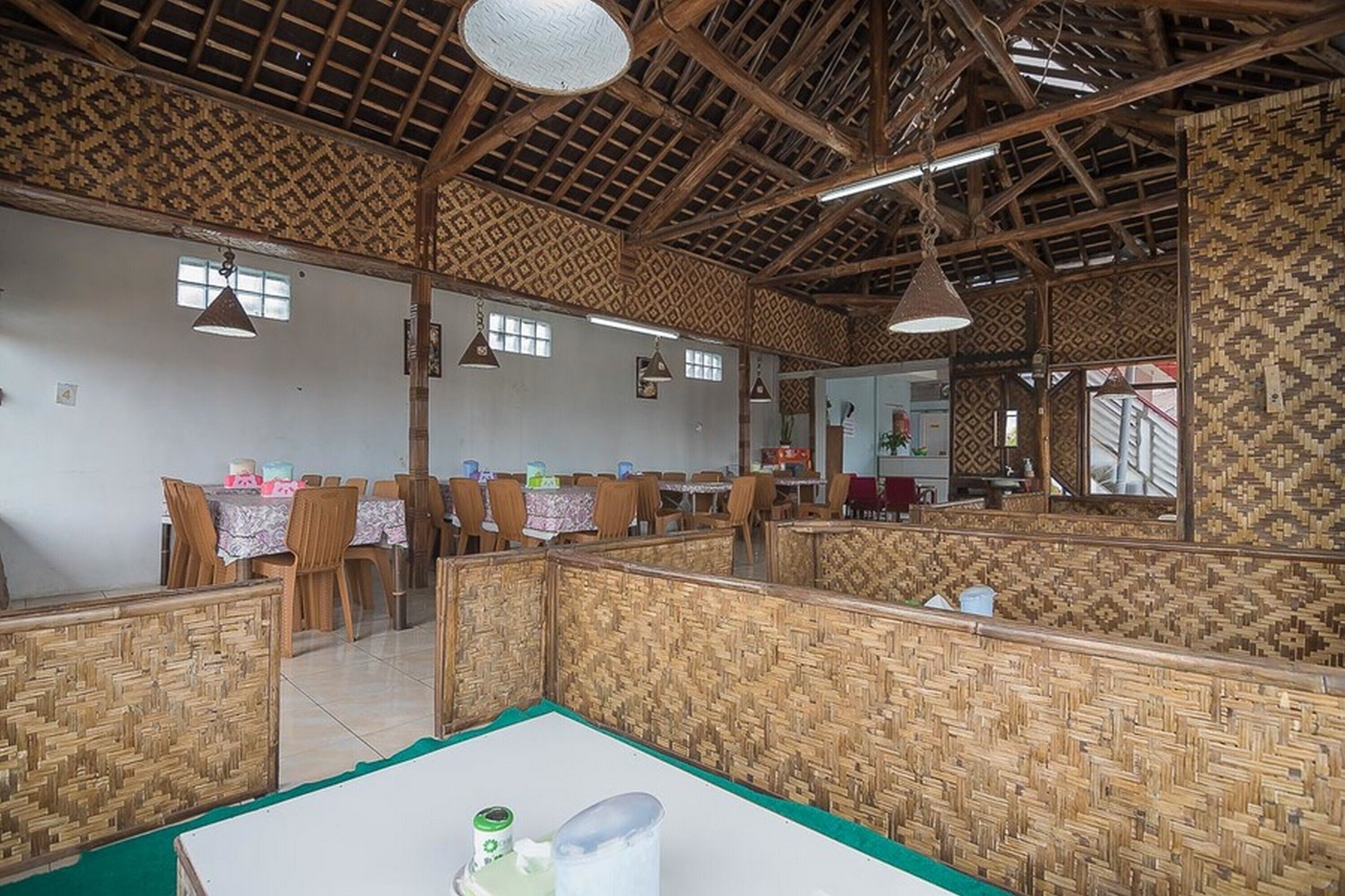 A restaurant with high wooden ceilings and woven partitions. Tables are set with chairs, and there are hanging lights.