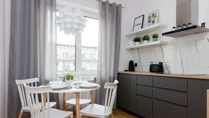 A modern kitchen with grey cabinets, a round dining table with white chairs, and a window with grey curtains. - Jerozolimskie Central View Apartment (Warsaw)