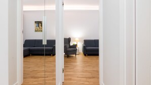 A modern living room with a wooden floor, two dark sofas, a small side table with a lamp, and a framed picture on the wall. - Jerozolimskie Central View Apartment (Warsaw)
